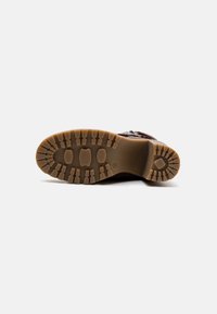 Suela de bota de goma marrón con profundas marcas para agarre, con un patrón de surcos distintivos y un talón redondeado. Superficie lisa y duradera.