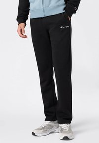 Pantalones de chándal negros hechos de una tela suave, con una cintura elástica y un logotipo bordado en blanco. Corte ajustado con piernas rectas y bolsillos laterales.