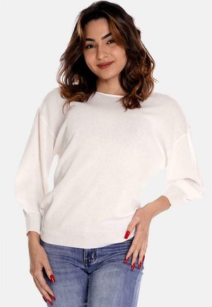 Maglione bianco a maglia con vestibilità morbida, spalle scese e polsini a coste, abbinato a jeans in denim blu. Texture liscia e design minimale.