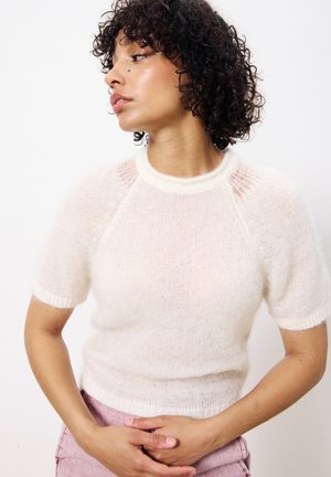 Top en tricot crème à manches courtes avec un col et des poignets côtelés ; tissu léger et texturé avec des pans transparents aux épaules.