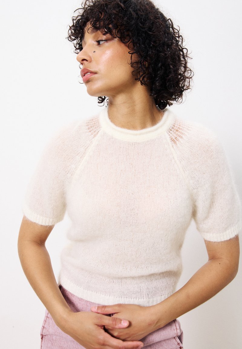 Cremfarbener, kurzärmeliger, gestrickter Pullover mit geripptem Halsausschnitt und Bündchen; leichtes, strukturiertes Material mit transparenten Paneelen an den Schultern.