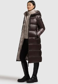 Long, shiny, dark brown puffer coat with a hood, featuring a smooth texture, zip closure, and elastic accents. Layered with a light beige inner jacket.