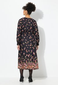 Blumenkleid in Midi-Länge aus schwarzem Stoff mit langen Ärmeln, gerafftem Bund und lebhaften Blumenmustern in Pink und Grün. Absatzschuhe.