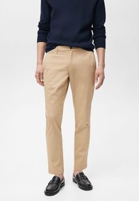 Beige chinos s slim prilegom, izdelani iz mešanice bombaža, dopolnjeni z mornarsko modrim puloverjem in črnimi loaferji. Imajo standardne žepke in gumbasto zapiranje.