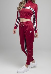 Rød træningsdragt sæt med kort zip-jakke og bukser med elastisk talje, der har sorte og hvide sidelister, glat tekstur og logodetalje.