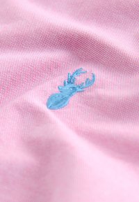 Pink fabric with a textured weave featuring a light blue embroidered stag design. The pattern is subtle and detailed.