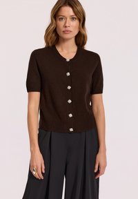 Brązowy kardigan z krótkim rękawem, okrągłym dekoltem, ozdobnymi guzikami i dopasowanym pasem. Gładki materiał dzianinowy o miękkiej teksturze.