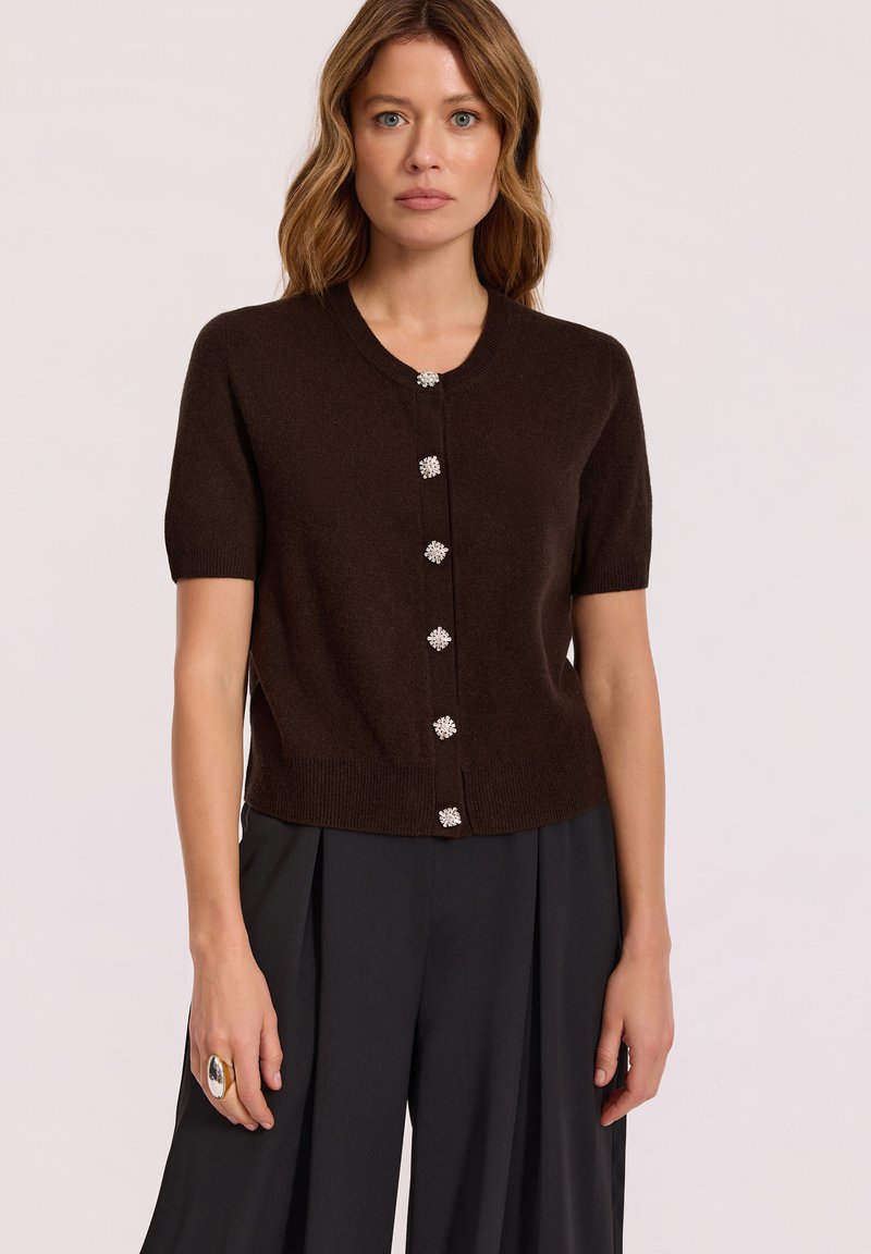Brązowy kardigan z krótkim rękawem, okrągłym dekoltem, ozdobnymi guzikami i dopasowanym pasem. Gładki materiał dzianinowy o miękkiej teksturze.