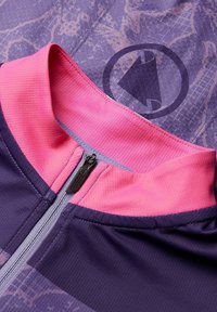 Haut de sport zippé violet et rose en tissu texturé, avec un col contrasté et un détail de logo circulaire.