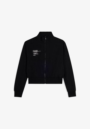 Veste noire zippée en tissu doux. Col montant, poignets et ceinture ajustés. Présente des impressions de texte blanc sur le côté gauche.