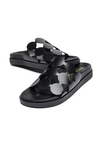 Sandales noires à semelle plate avec un motif de fleurs découpées, en matériau synthétique, et une légère texture. Détail logo doré sur la semelle intérieure.