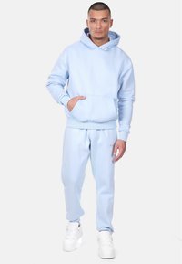 Light blue hoodie with kangaroo pocket and ribbed cuffs, paired with matching joggers. White sneakers complete the outfit.