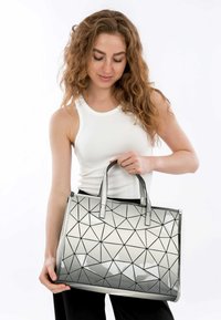 Silberne geometrische Handtasche mit glänzender Oberfläche, die mit dreieckigen Mustern, doppelten Griffen und einer strukturierten rechteckigen Form ausgestattet ist.