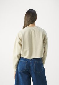 Felpa beige cropped con spalle cadenti, realizzata in tessuto morbido. Indossata con jeans a gamba larga blu scuro con tasche posteriori.