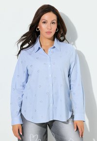 Hellblaues Hemd mit Knöpfen und vertikalen Streifen, versehen mit silbernen, bestickten Blumenmustern; lange Ärmel mit geknöpften Manschetten.