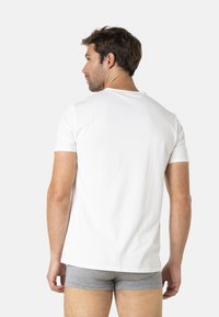 T-shirt en coton blanc à manches courtes et col rond, vu de dos. Short gris ajusté visible en dessous.