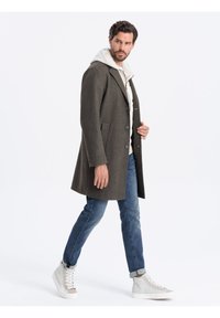 Manteau en laine gris avec une coupe ajustée, revers crantés et boutons à l'avant. Associé à un jean bleu clair et des baskets montantes grises.