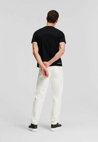 Camiseta negra de manga corta, pantalones blancos, zapatillas altas. Diseño sencillo con un pequeño logo en la parte inferior. Fondo neutro.