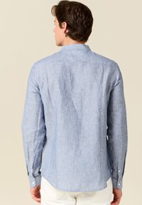Camicia a maniche lunghe a righe blu con colletto, dettagli con bottoni sui polsi e un orlo leggermente curvo, realizzata in tessuto leggero.