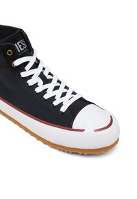 Černé vysoké tenisky s bílými tkaničkami, bílým gumovým špičkovým krytem, hnědou podrážkou a červeným pruhem podél okraje podrážky.