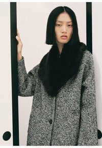 Cappotto in misto lana con motivo houndstooth, caratterizzato da un colletto in pelliccia nera. Il cappotto ha una vestibilità ampia e chiusura con bottoni, posto su uno sfondo neutro.