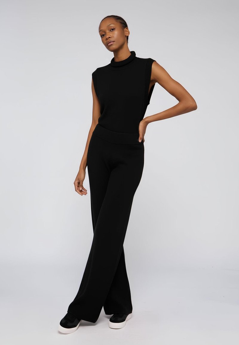 Czarna bezrękawnikowa bluzka z kołnierzykiem w stylu golf, zestawiona z szerokimi czarnymi spodniami. Gładki materiał z teksturowanym dekoltem, dopełniona czarnymi trampkami.