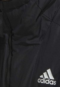Chaqueta negra aislante con cremallera frontal, que presenta un logo blanco de Adidas y una tela suave y ligera.