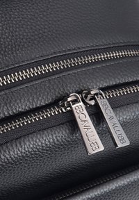 Zwarte leren tas met twee metalen ritsen met gegraveerde trekstangen, een gestructureerd oppervlak en contrasterende stiksels langs de naden.