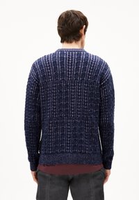 Navy blauwe gebreide trui met textuur en geribbelde patronen, ronde halslijn en aangesloten cuffs. Het materiaal lijkt dik en warm, geschikt voor koudere weersomstandigheden.