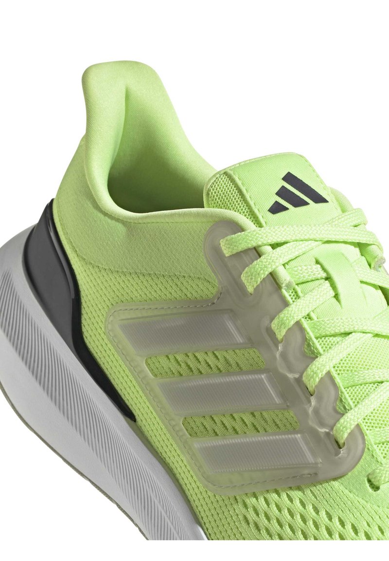 Zapatilla deportiva verde lima con parte superior de malla, cuello acolchado y suela de goma blanca; cuenta con un logotipo de tres franjas transparente y cordones texturizados.