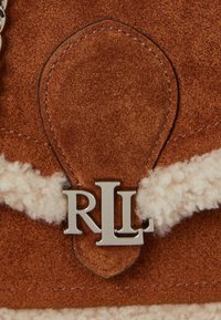 Borsa a tracolla in suede marrone con dettagli in shearling crema; presenta un logo "RLL" argentato su un pattina arrotondata. La cucitura è visibile lungo i bordi.