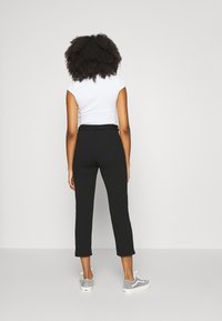 Svarta skräddarsydda byxor i ankle-length med en slät yta, hög midja, framfickor och uppvikta fållar, ihop med en åtsittande vit topp och grå sneakers.