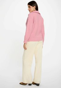 Maglione rosa a maglia con colletto, caratterizzato da un motivo testurizzato. Abbinato a pantaloni in corduroy larghi color crema e tacchi marroni.