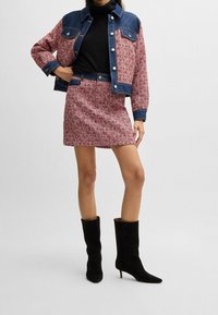 Jeansjacka med röd- och vitvävd mönster, kombinerad med en matchande vävd kjol. Svarta knähöga stövlar. Texturkontraster mellan materialen.