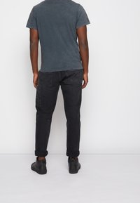 Tmavě šedé tričko s krátkým rukávem, z bavlněné směsi, s mírně vybledlou texturou, doplněné černými kalhotami s ohrnutými manžetami a černými botami.