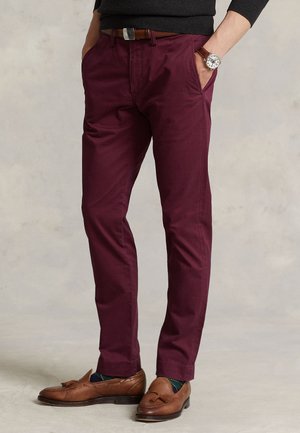 Homme portant un pantalon slim bordeaux, une ceinture en cuir marron, des mocassins à glands marron et une montre-bracelet avec un bracelet en cuir marron.