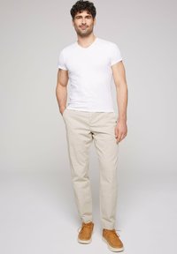 T-shirt en coton blanc à col en V, chinos beige clair et baskets en daim tan. L'ensemble présente une coupe décontractée et un design minimaliste.