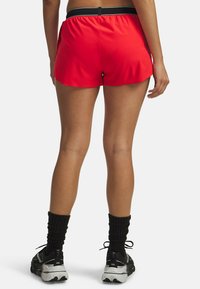 Shorts atléticos rojos con una banda en la cintura negra, hechos de un material ligero, con un diseño ligeramente acampanado y una textura suave.