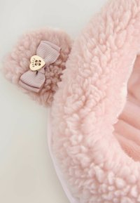 Rosa fluffig textil med en mjuk textur. Har en ljusrosa rosett med en guldhjärtanhängen som förbättrar dess design. Rund form.
