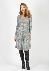 Szara sukienka kopertowa z czarno-białym wzorem w formie wiru, z długimi rękawami i rozkloszowaną spódnicą. Do niej czarne skórzane kozaki za kolano.