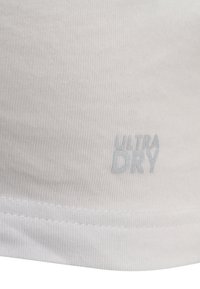Vitt tyg med en slät yta som har ljusblått broderad text "ULTRA DRY" nära fållen. Enkelt och minimalistiskt design.