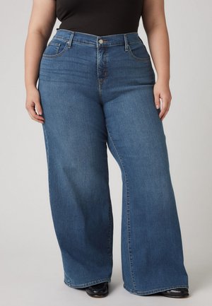 Vide bened jeans i en middels blå vask, med frontlommer, knappestang og et glatt, teksturert stoff.