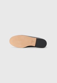 Black shoe sole with a smooth, light brown base. Features a slight heel and minimal tread pattern. Textured surface along the edges.