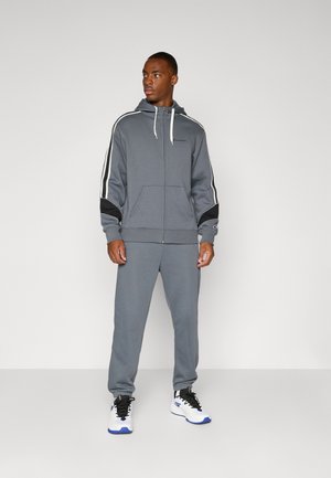 Felpa grigia con zip e pantaloni coordinati realizzati in tessuto morbido. La felpa presenta dettagli neri e strisce bianche lungo le maniche.