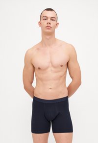 Marineblaue Baumwoll-Boxershorts mit einem weichen elastischen Bund, figurbetontem Design und einem zentralen Beutel für Unterstützung. Glatte Textur und minimale Nähte.