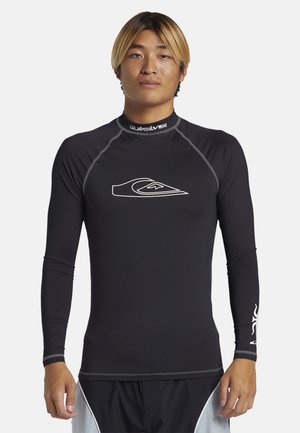 Čierny dlhý rukáv rashguard s plochými švami, vysokým golierom a bielym logom na hrudi. Vyrobený z elastického materiálu, ktorý odvádza vlhkosť.