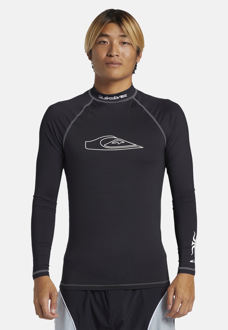 Černý dlouhý rukáv rashguard s plochými švy, vysokým límcem a bílým logem na hrudi. Vyrobeno z pružné, vlhkost-odvádějící látky.