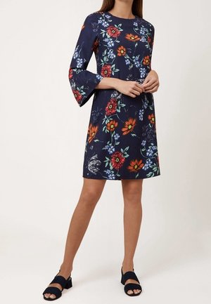 Abito floreale blu navy con maniche a campana, caratterizzato da fiori rossi e blu, vestibilità comoda, lunghezza al ginocchio, abbinato a sandali scuri.