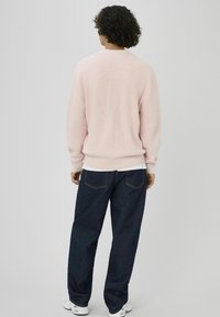 Pull en maille côtelée rose clair avec un col rond, associé à un jean bleu foncé ample. La tenue présente un design superposé.