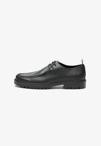 Zapatos de cuero negro con un acabado suave, punta redondeada y costuras decorativas. Cuenta con una suela de goma con surcos para tracción y un diseño de cordones.